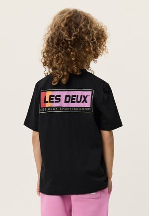 Fekete pamut póló, a hátoldalán rózsaszín és narancssárga árnyalatú téglalap alakú logóval, rövid ujjú és laza szabású.