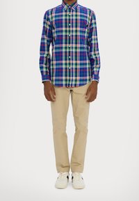 Flerfärgad rutig skjorta i blått, grönt, vitt och rött, med krage som knäppes. Kombinerad med khakifärgade byxor och vita sneakers.