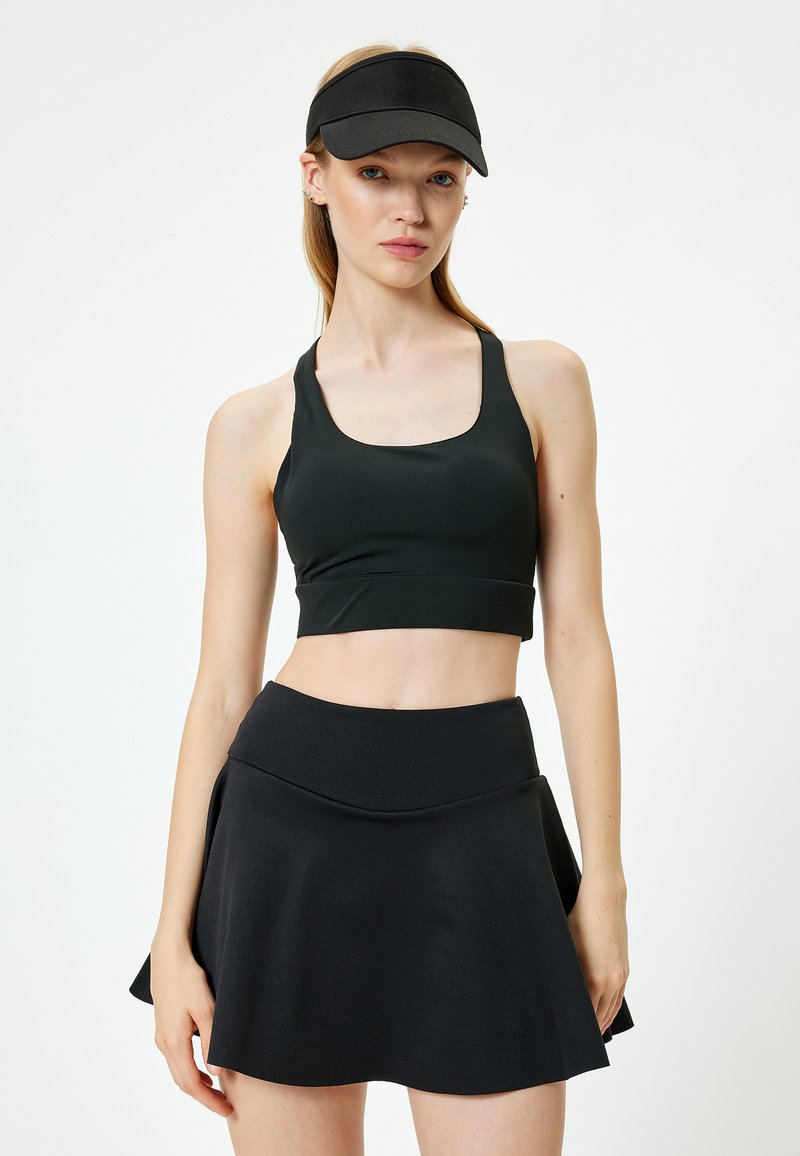 Musta urheilullinen crop-top leveillä olkaimilla, yhdistettynä matching flare-hameeseen. Suuri tekstuuri, minimaalinen muotoilu ja ei näkyviä kuvioita tai yksityiskohtia.