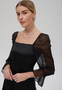 Mustmust dress, millel satinist bodice ja läbipaistvad puffvarrukad, ruuduline kaelus ja volditud detailid varruka mansettides. Hõbedased ehted aktsentideks.