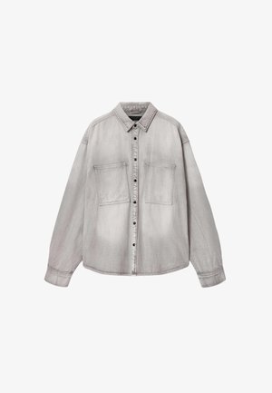 Chemise boutonnée gris clair à manches longues, avec deux grandes poches poitrine sur le devant et un col classique, présentée à plat sur un fond blanc.