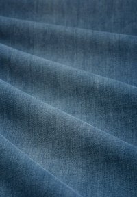 Denimstof in een middenblauwe tint, met een zachte textuur en diagonale weefpatronen en subtiele kleurvariaties.