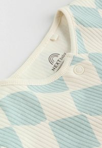 Könnyű, bordázott anyagú kezeslábas, krémszínből készült, váltakozó világoskék és krémszínű rombusz mintával. Nyomógombbal és címkével rendelkezik.