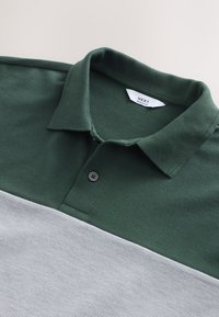 Zöld és szürke csíkos pólóing texturált anyagból, galléros nyakkal, kétgombos elülső résszel és hozzávarrt márkajelzéssel.