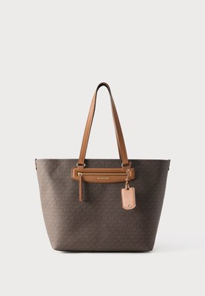 Rjava torbica Michael Kors tote z dolgimi rjavimi ročaji, žepom z zadrgo na sprednji strani in pripeto usnjeno značko, postavljena na enakomerno belo ozadje.