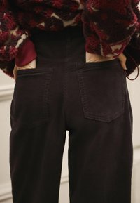 Black corduroy pants with a ribbed texture, featuring two back pockets and a high waist, paired with a fuzzy patterned sweater.