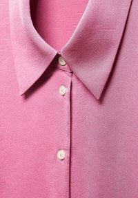 Chemise rose à col avec une texture lisse, dotée d'une patte de boutonnage et de boutons de couleur claire, présentant une teinte uniforme et un tissu doux.