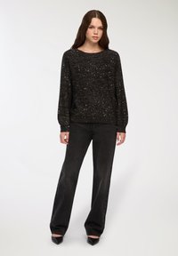 Czarny sweter o strukturalnym wzorze, z metalicznymi drobinkami. W połączeniu z czarnymi, wysokim stanem spodniami z szerokimi nogawkami oraz czarnymi, szpiczastymi szpilkami.