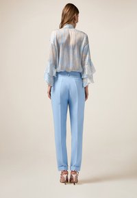 Helles, blaues, tailliertes Hosen, mit einer glatten Textur, kombiniert mit einer halbtransparenten, gemusterten Bluse mit Rüschensäumen in sanften Pastellfarben.