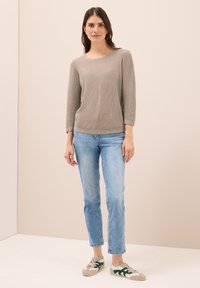 Hellgrauer, gestrickter Pullover mit rundem Ausschnitt und Dreiviertelärmeln, kombiniert mit hellblauen Jeans und grauen Sneakers mit grünen Akzenten.
