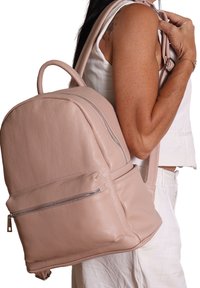 Zaino in pelle rosa chiaro con forma arrotondata. Presenta una tasca frontale con zip e una superficie testurizzata. Visibili le cinghie regolabili e il manico superiore.