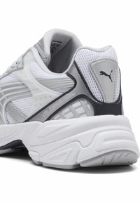 Baskets de sport blanches et grises avec tige en maille, semelle rembourrée, accents texturés et détail de marque au niveau du talon.