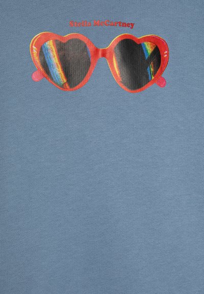 Mėlynas audinys su raštu raudonų širdies formos saulės akinių, turinčių tamsius lęšius ir vaivorykštės akcentus, užrašu "Stella McCartney".