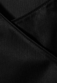 Tissu noir présentant un motif discret en chevron, une texture lisse et des plis diagonaux, avec des coutures visibles le long des bords.