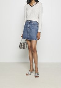 Kremowy sweter z dekoltem w serek, dżinsowa mini spódniczka, srebrne buty na slip-on, oraz szara torebka we wzór węża z łańcuchowym paskiem. Gładkie tekstury.