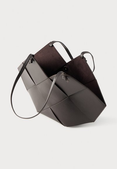 Sac fourre-tout en cuir gris foncé avec un design patchwork tissé, ouverture supérieure et fines bandoulières, sur un fond clair uni.