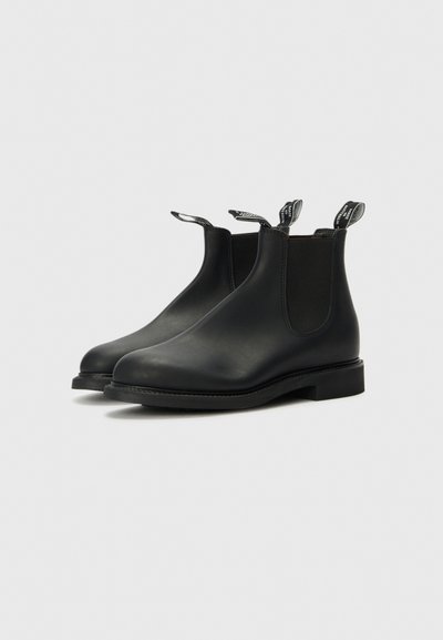 Svarta läderankelboots med elastiska sidopaneler, rundade tår och bakre dragflikar. Har en låg, platt sula och minimalistisk design.