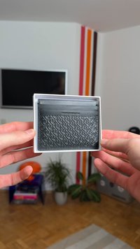 Melnas ādas kartes turētājs ar reljefa rakstu, kas satur piecas kartes vietas un ir eleganti taisnstūrveida formas. Iepakots baltā kastē.