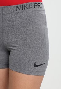 Szare sportowe spodenki z czarnym logo Nike i napisem „NIKE PRO” na pasku. Wykonane z dopasowanej, teksturowanej tkaniny.