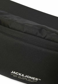 Sort stof crossbody tas med glat tekstur, udstyret med en top lynlås lukning og et fremtrædende "JACK & JONES" logo trykt i hvid.