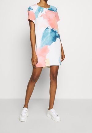 Woman wearing a short-sleeve, above-knee dress with abstract pink, blue, and white watercolor pattern, paired with white platform sneakers.