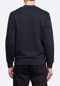 Felpa blu navy con scollo a girocollo, polsini e vita a costine. Presenta strisce bianche sui polsini delle maniche. Texture del tessuto morbida.