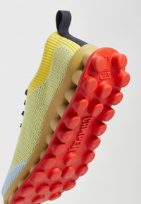 Yellow and green knitted upper with navy accents, flexible rubber sole featuring prominent red traction knobs. Brand name "CAMPER" embossed.