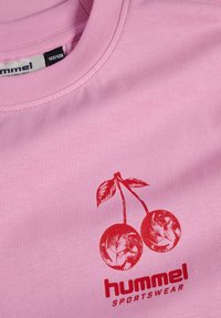 Rosa bomullströja med en röd körsbärsgrafik och texten "hummel SPORTSWEAR", med ribbat rundhals och slät textur.