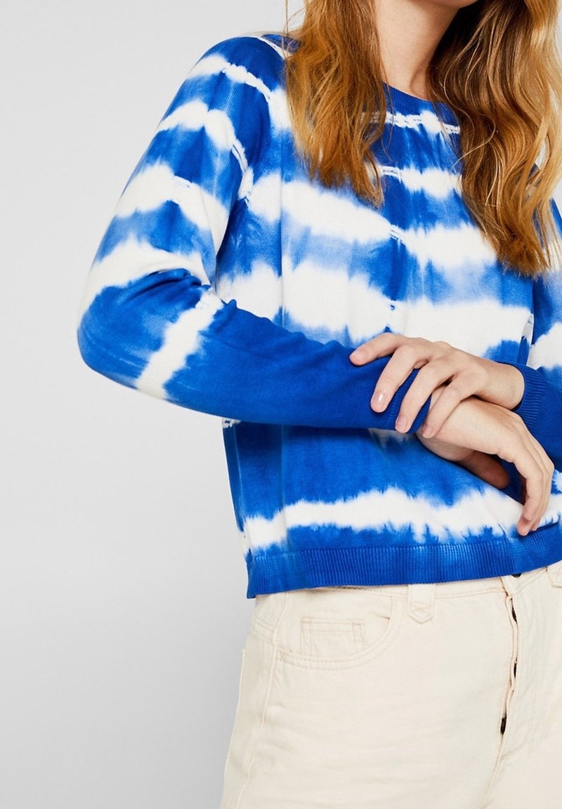 Sininen ja valkoinen batik-värjätty collegepaita, jossa pyöreä pääntie ja resorit hihansuissa. Pehmeää kangasta ja rento istuvuus. Vaaleansävyiset housut näkyvissä.