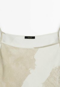 Haut sans manches léger présentant un mélange de motifs abstraits beige et blancs, avec un tissu semi-transparent et des bretelles ajustables. Étiquetage noir à l'intérieur.