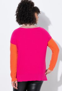Maglione a girocollo con un corpo rosa, maniche arancioni e un colletto a coste color beige. L'orlo è leggermente arricciato e la texture sembra morbida.