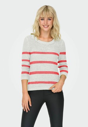 Helles graues Strickpullover mit roten horizontalen Streifen, runder Ausschnitt und Dreiviertelärmel. Kombiniert mit schwarzen, enganliegenden Hosen.