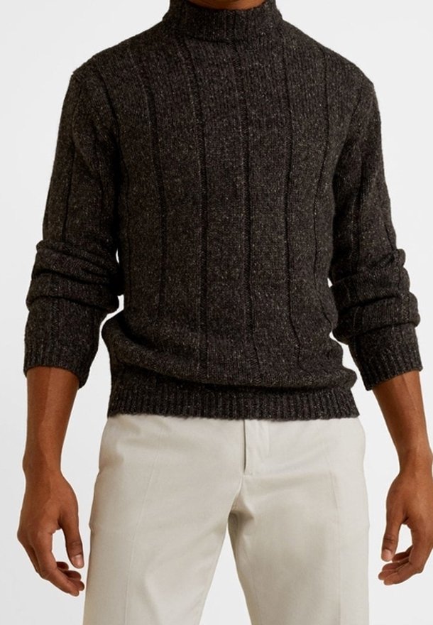 Pull en maille gris foncé avec un col montant, présentant une texture côtelée verticale et des poignets flexibles, associé à un pantalon de couleur claire.