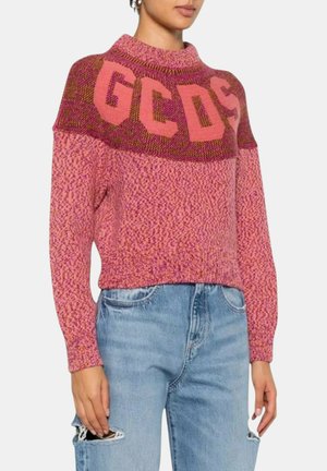Donna che indossa un maglione lavorato a maglia rosa e viola con la scritta "GCDS" sulla parte superiore, abbinato a jeans strappati azzurri chiari.