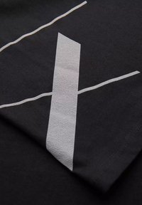 Černé tričko z látky s texturovaným bílým grafickým designem, který obsahuje dvě kontrastní linie. Materiál vypadá měkký s hladkou texturou.