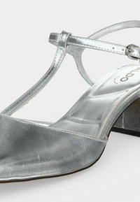 Sandale en cuir métallisé argent à talon bas, bride en T et fermeture à boucle, semelle intérieure rembourrée et talon bloc.