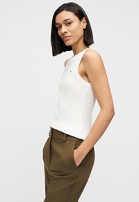 Λευκό αμάνικο τοπ με στρογγυλή λαιμόκοψη και μικρό λογότυπο. Συνδυάζεται με χακί παντελόνια ψηλόμεσα, με πλαϊνές τσέπες.
