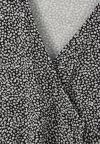 Tejido negro con un pequeño patrón floral blanco, que presenta un diseño envolvente y una textura suave. Bordes lisos y detalles de costura mínimos.