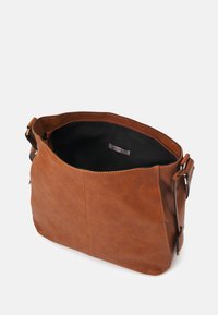 Brązowa skórzana torba na ramię z przestronnym wnętrzem, kontrastową czarną podszewką i jednym regulowanym paskiem. Posiada eleganckie detale w postaci szwów.