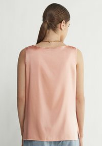 Satin rygglös ärmlös topp i mjuk rosa. Har en rund halsringning och sidofickor för enkel rörelse. Slät textur med minimal detaljering.