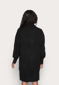 Svart stickad klänning med hög polokrage, lösa ärmar och en något avsmalnande nederkant. Mjuk textur och minimalistisk design.