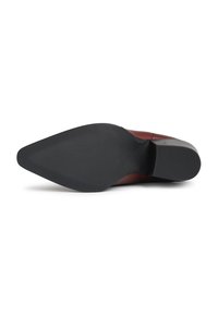 Zapato de cuero marrón con punta afilada visto desde abajo, destacando una suela negra texturizada y un tacón bajo tipo bloque.