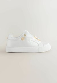 Bela nizka superga z zavezovanjem iz satenskih trakov, okrašena z biseri in zlatimi kroglicami ter majhno zlatim srcem kot obeskom na strani.