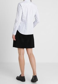 Camicia bianca a maniche lunghe con motivi, abbinata a una gonna nera con taglio dritto e dettagli delle cuciture visibili. Scarpe nere robuste completano il look.