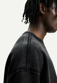 Black sweatshirt with a soft texture, featuring a crew neck, visible stitching details, and a relaxed fit, captured from a side angle.