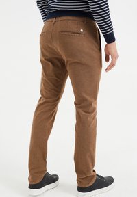 Brązowe, plecione spodnie o teksturowym wykończeniu, z dwoma tylnymi kieszeniami i guzikiem jako detalem. Połączone z czarnymi trampkami i pasiastą bluzką.