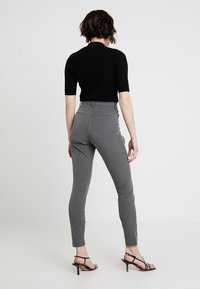 Harmaat räätälöidyt housut, joissa on slim fit -leikkuu ja keskikorkea vyötärö, takataskuilla varustettuna. Yhdistetty tiukkaan mustaan lyhythihaiseen paitaan.