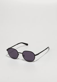 Ochelari de soare negri cu lentile ovale întunecate, cadru din metal, brațe subțiri și tampoane nazale transparente. Caracterizează un design minimalist, fără accente decorative.