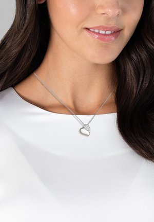 Silver heart pendant necklace with a polished finish and a textured section featuring small stones, worn on a silver chain against a white top.