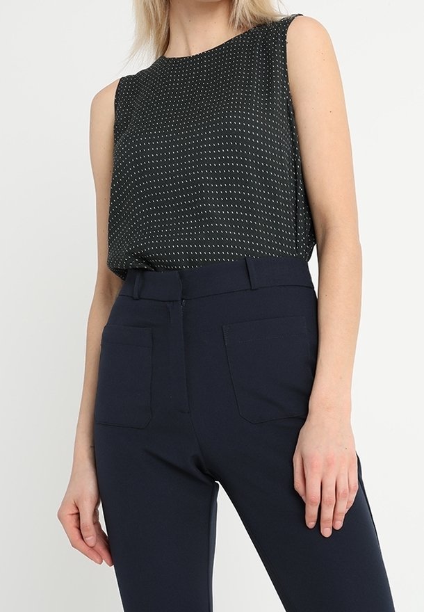Svart ärmlös topp med vitt prickigt mönster, tillsammans med marinblå högmidjade byxor med två bakfickor och en mjuk tygtextur.